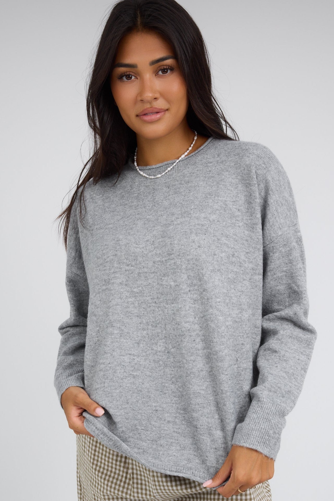 Young woman wearing a grey pullover with a rolled neckline and long sleeves.