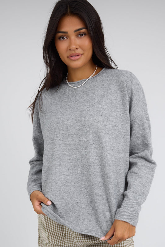 Young woman wearing a grey pullover with a rolled neckline and long sleeves.