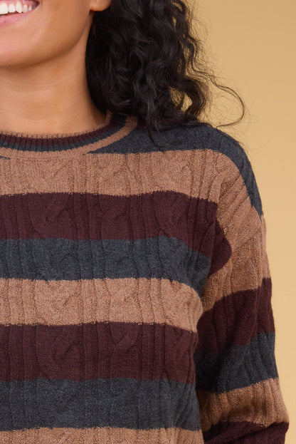Close viewof a woman wearing a 3 color stripe, cable knit long sleeve sweater.