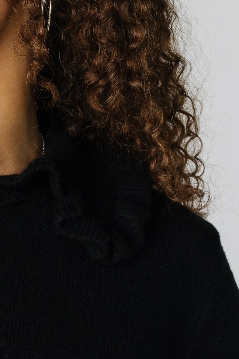 Close view of a woman wearing a black sweater with a wide ruffle collar