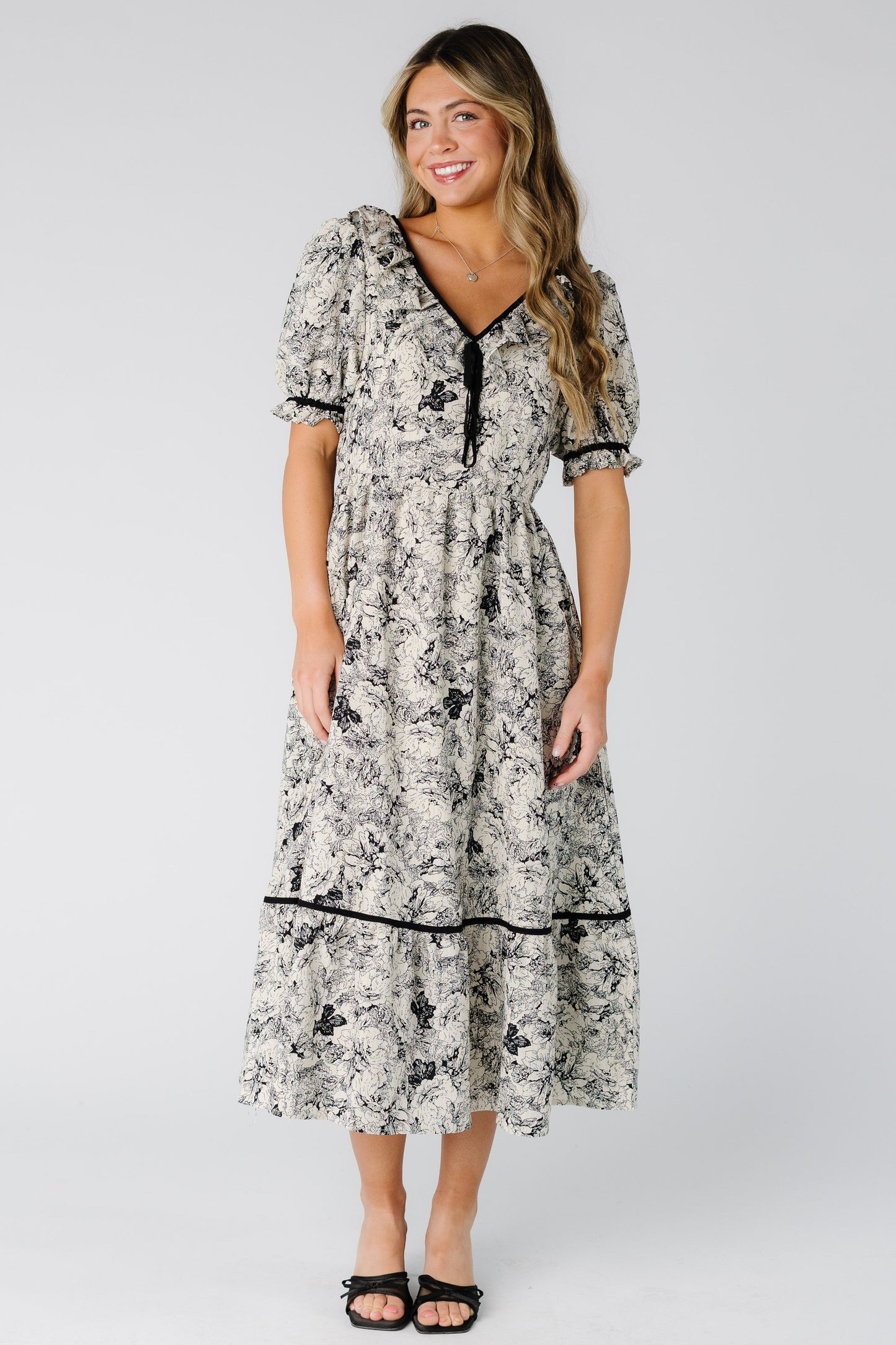 Woman wearing a black and  white print midi dress with a full gathered skirt 