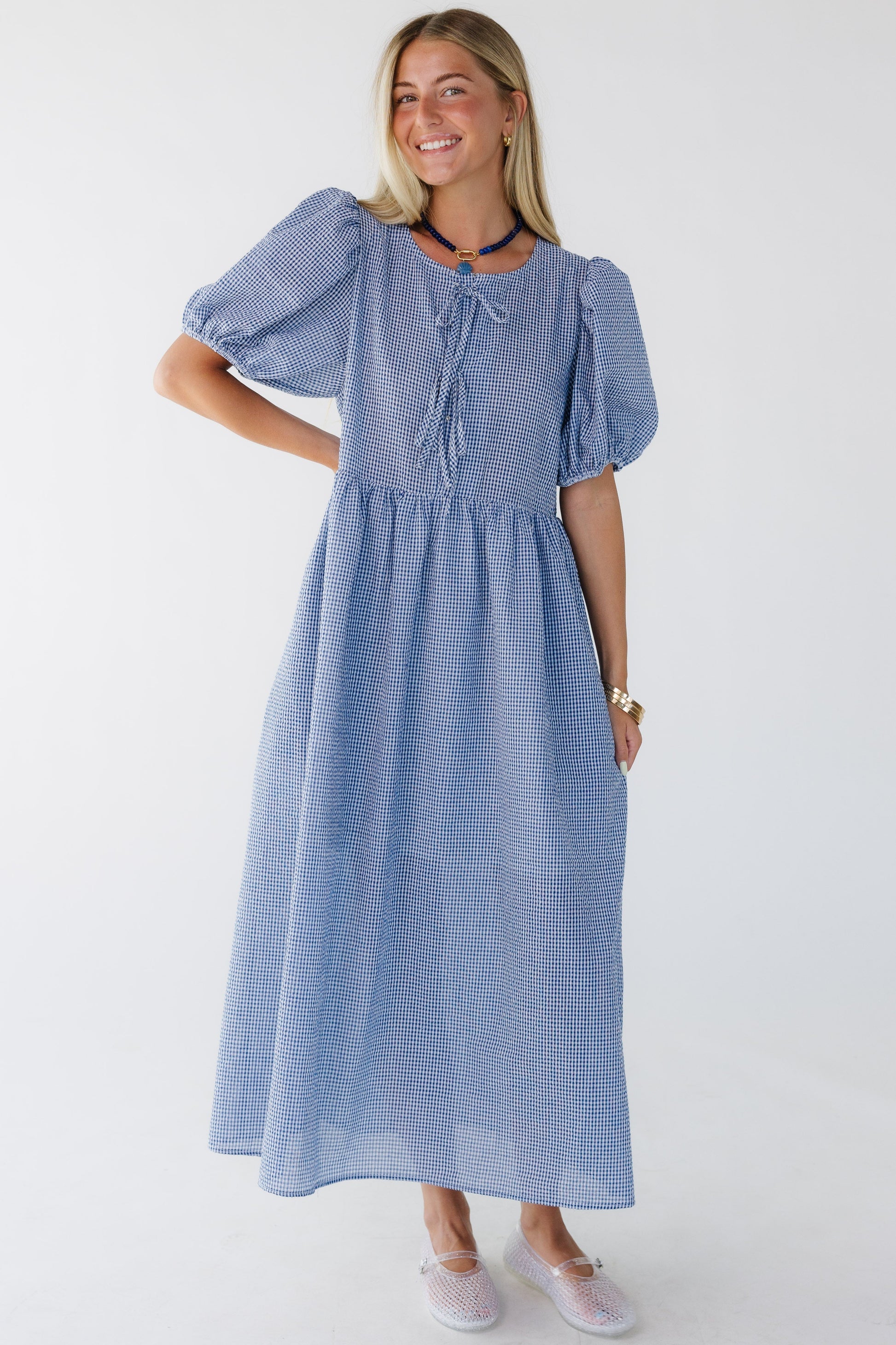 Young woman wearing a blue & white textured, loose fitting midi dress with a round neckline, and large balloon sleeves.