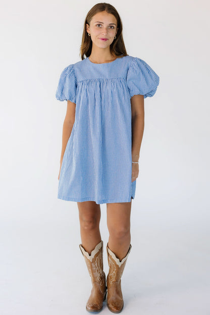 Young woman wearing a short blue and white baby doll dress with a short yoke and large puff sleeves.