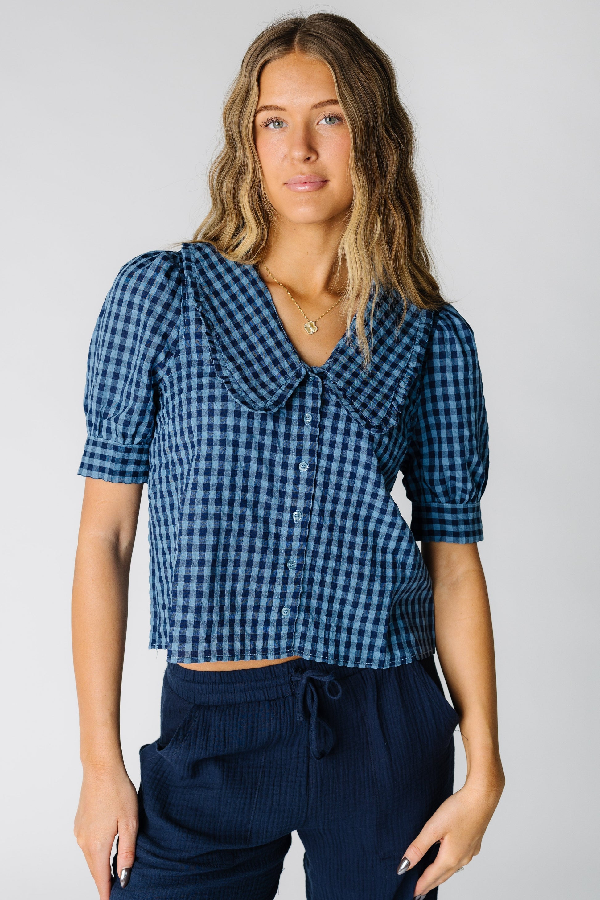Woman wearing a navy gingham button down top with a V-neckline with a wide collar