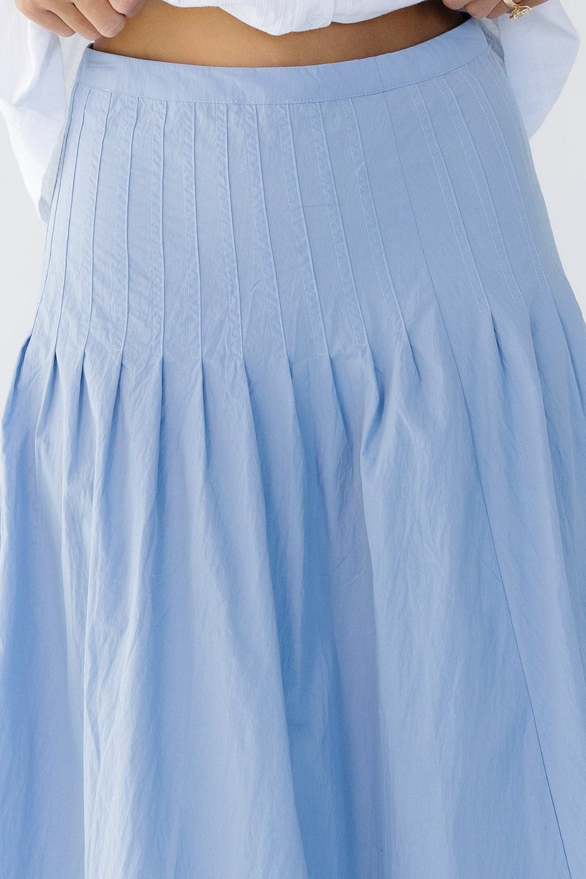 Close view of a young woman wearing a blue skirt with sewn down pleats all around the hip.