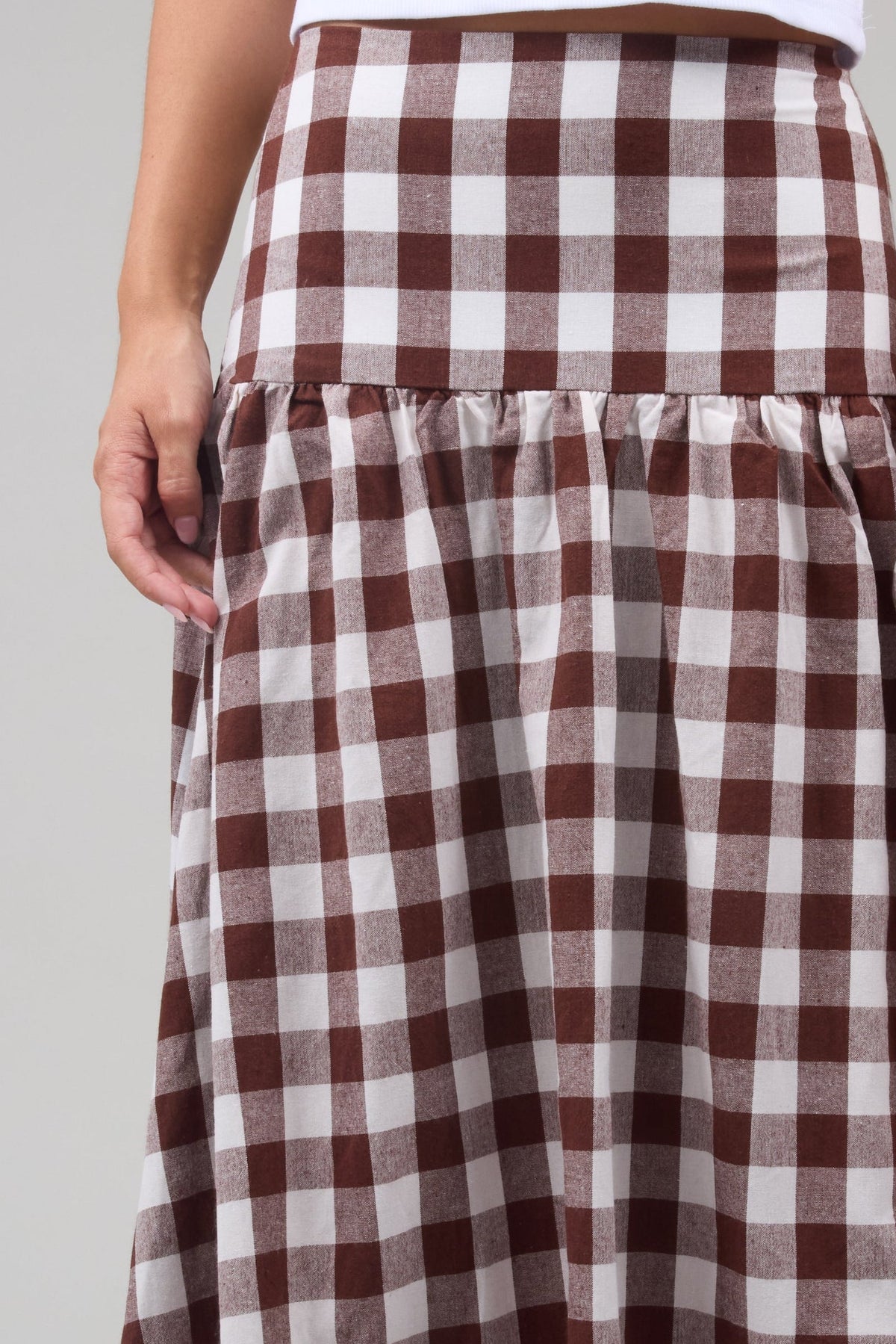 Close view of a woman wearing a brown and & white large gingham print, drop waist skirt.