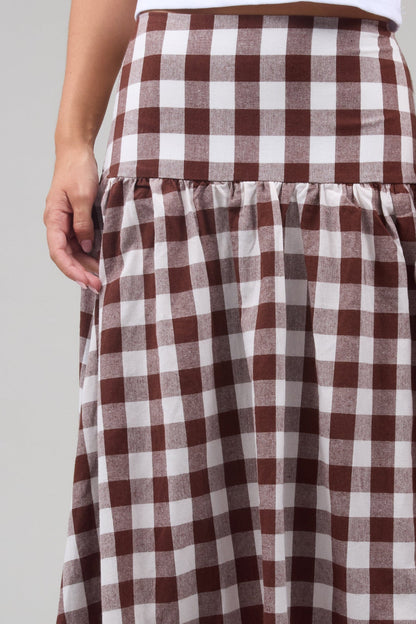 Close view of a woman wearing a brown and & white large gingham print, drop waist skirt.