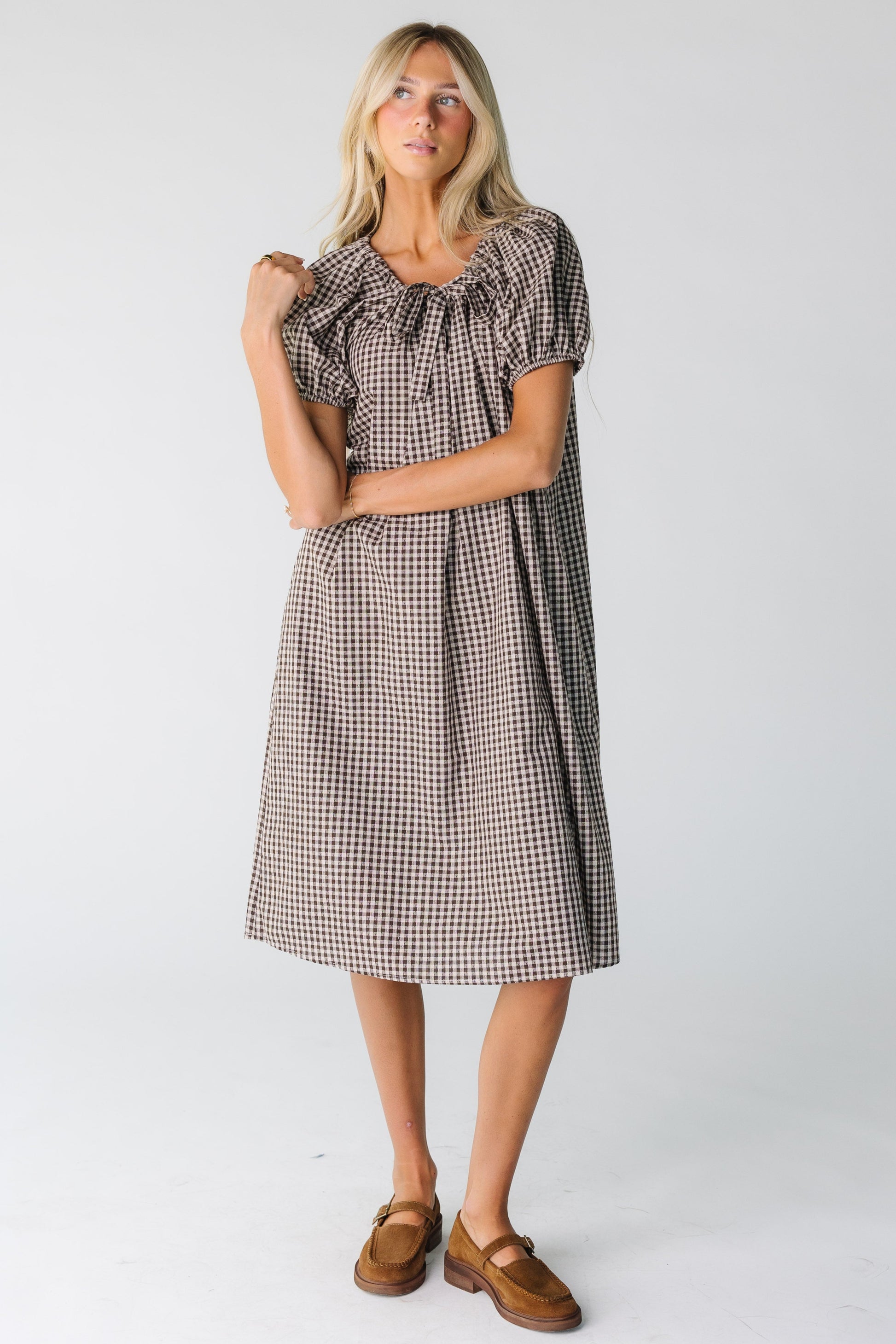 A woman in a brown gingham midi dress with short sleeves