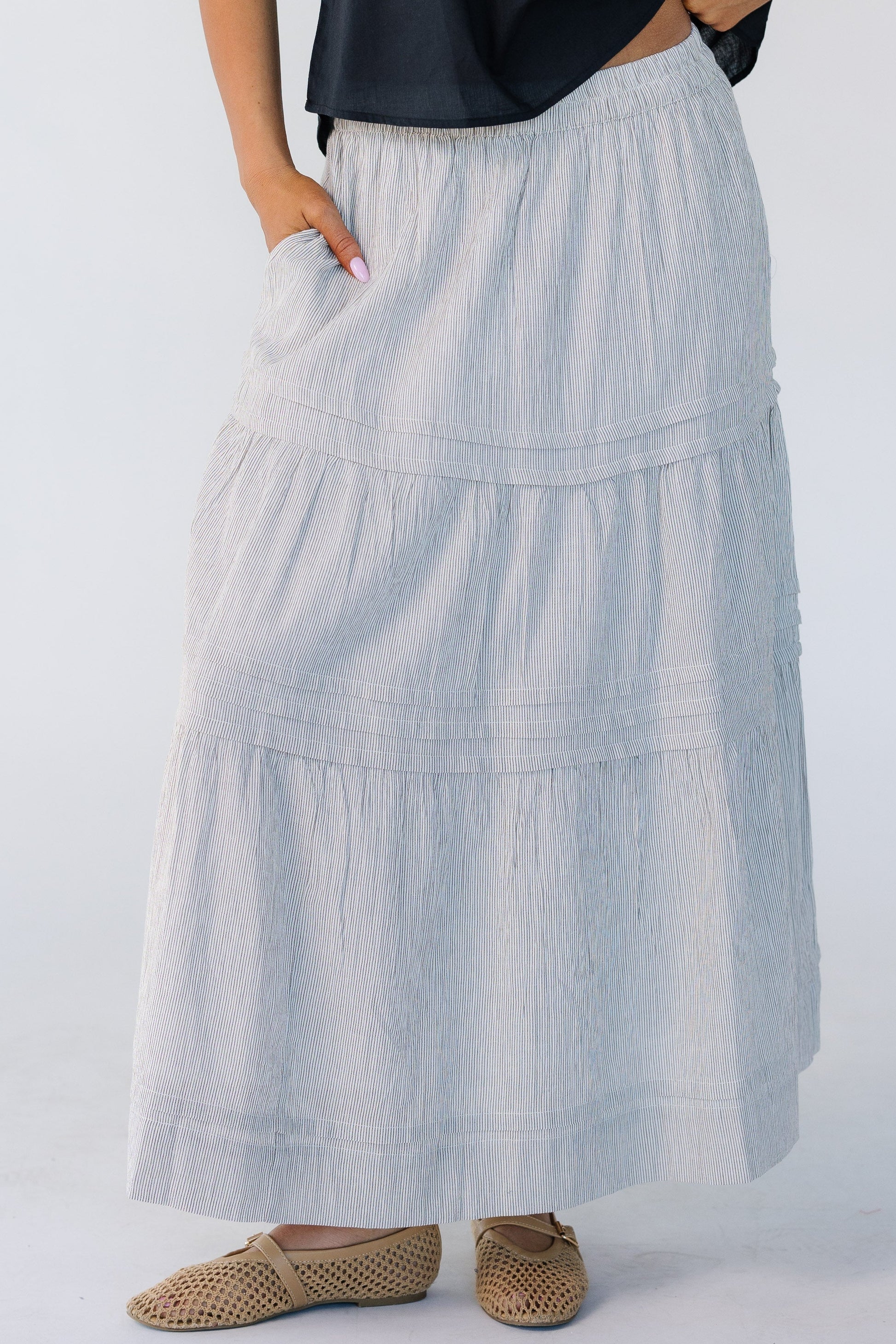 Woman wearing a modest narrow brown stripe midi skirt with tiers and horizontal pleats.