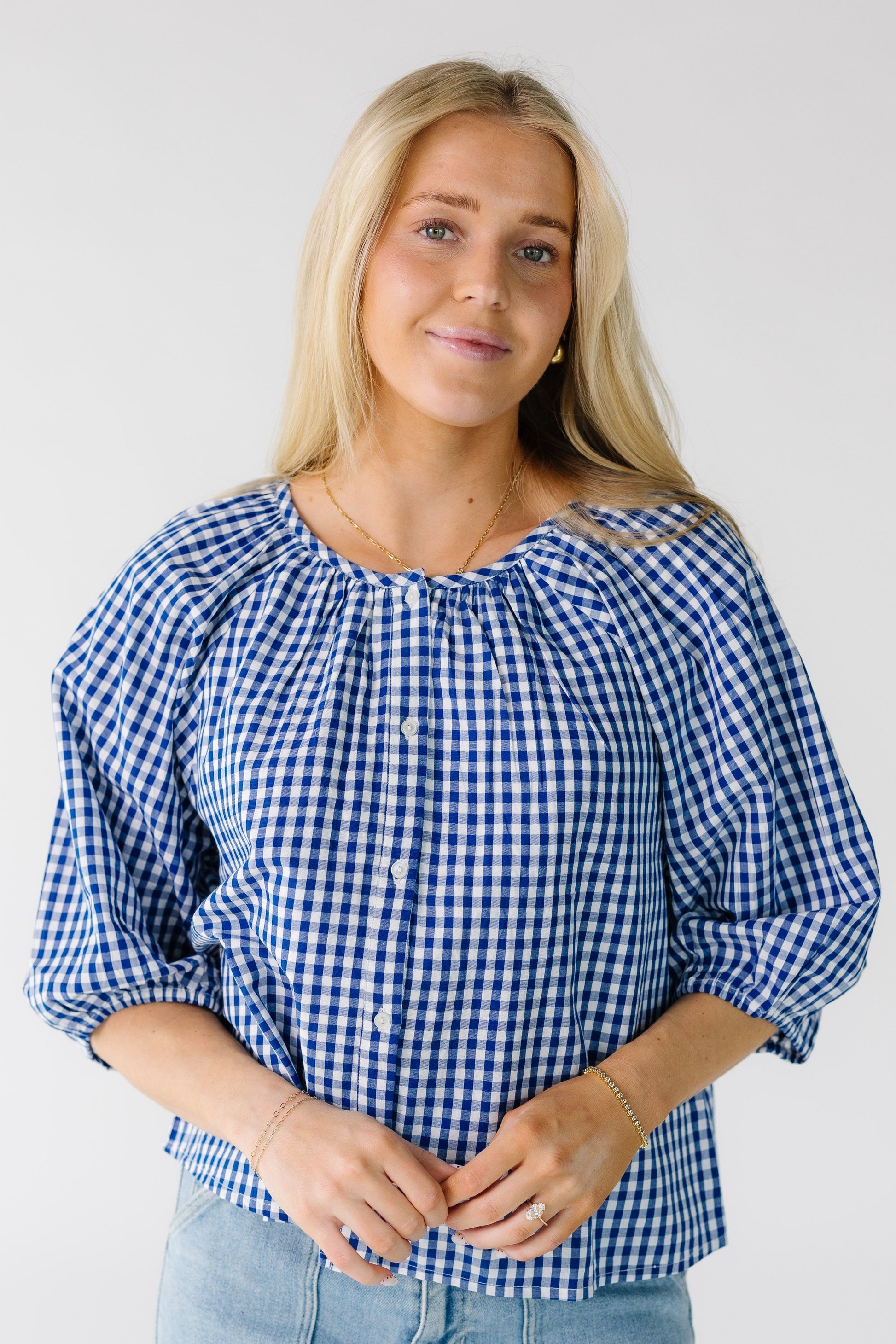 Woman wearing a white and blue gingham button down blouse with half length puff sleeves.