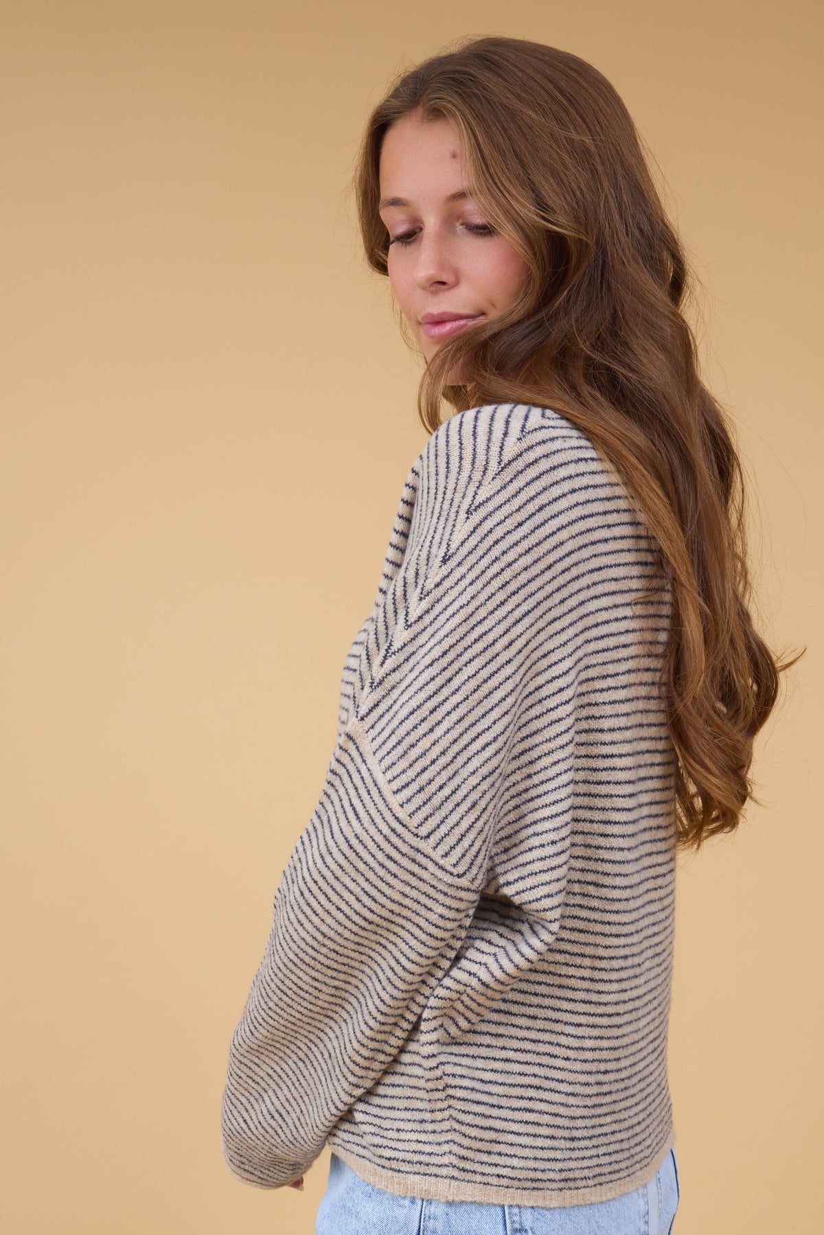 A side view of a woman wearing a loose fitting natural & black sweater with long sleeves.
