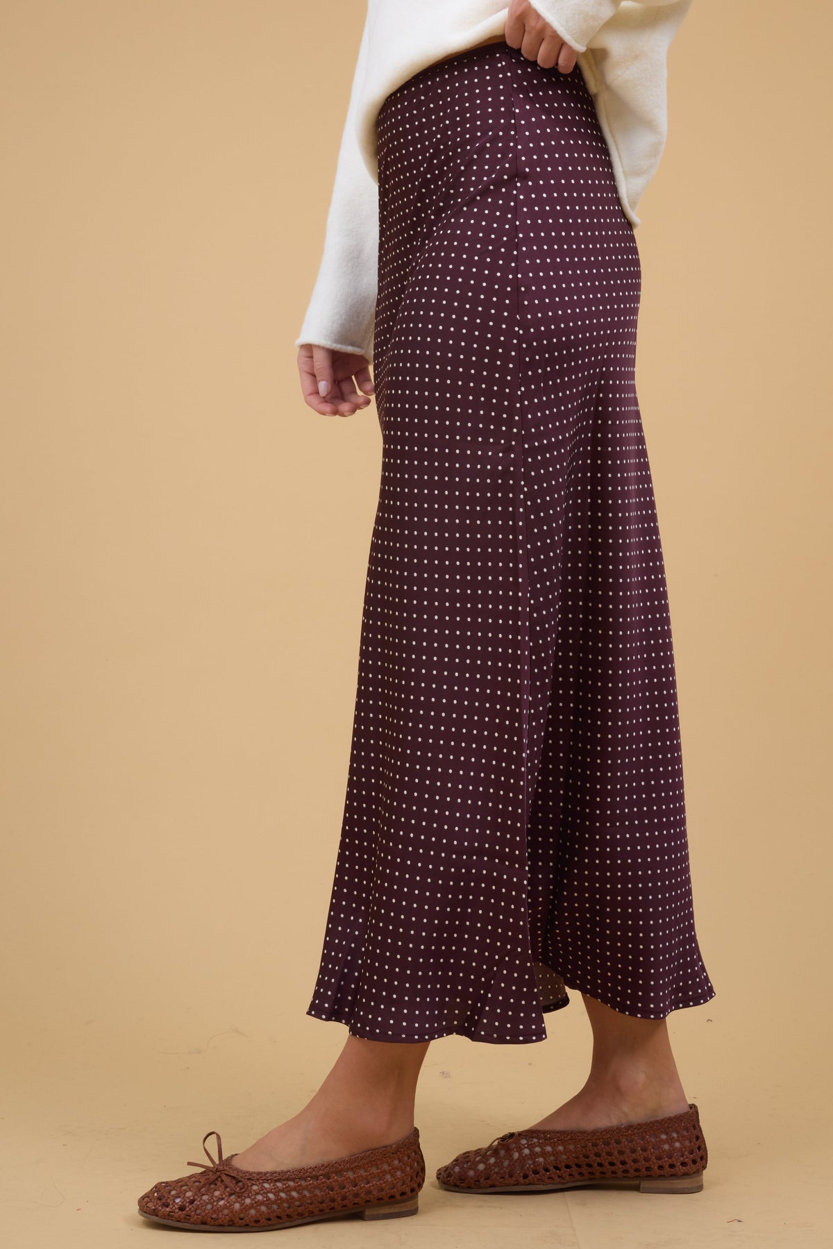 Side view of a woman wearing a A-line midi skirt in brown with white polka dots.