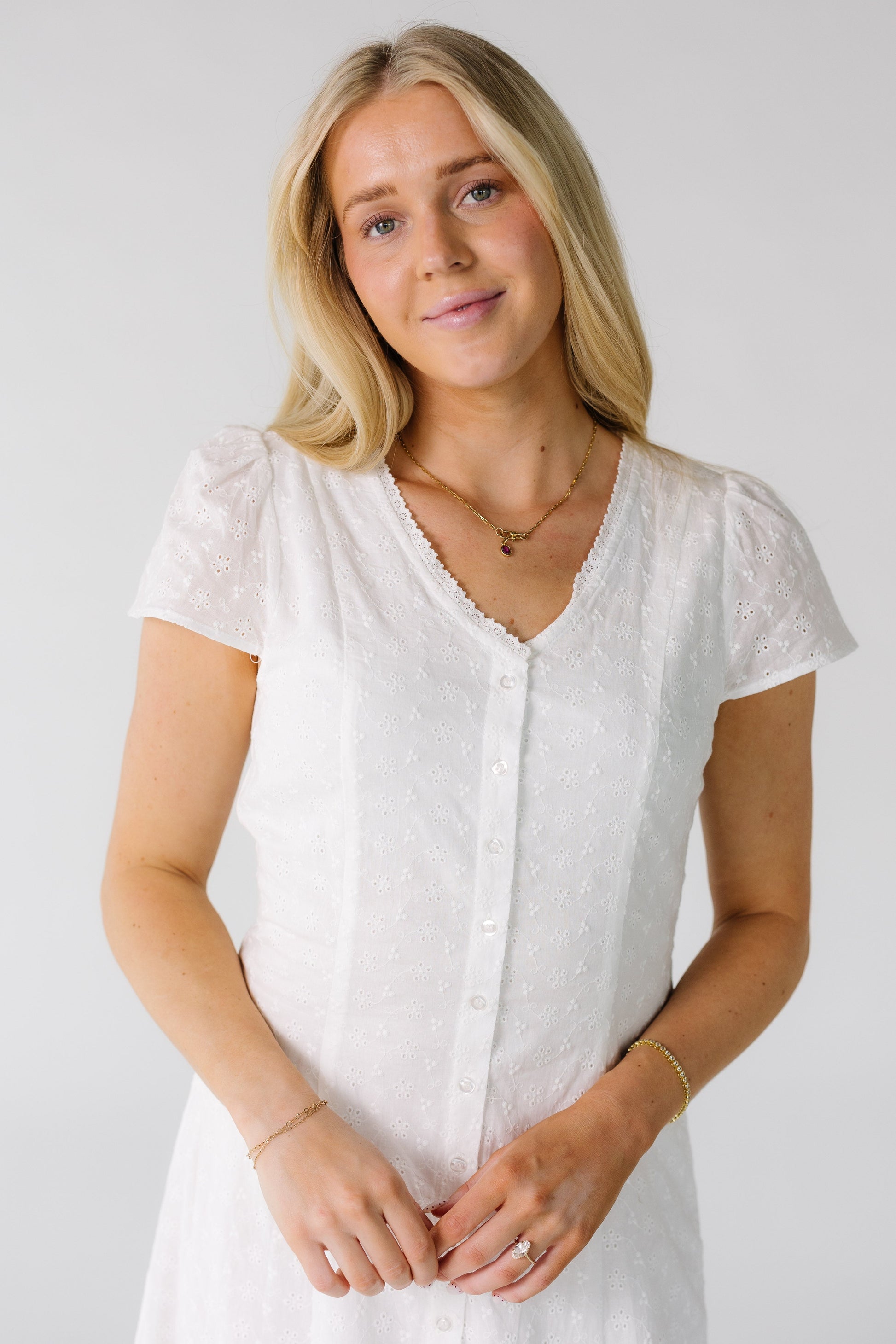 Close view of a woman wearing a white all eyelet button down dress with a -neckline and short puff sleeves.