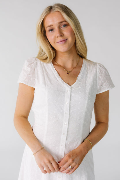 Close view of a woman wearing a white all eyelet button down dress with a -neckline and short puff sleeves.