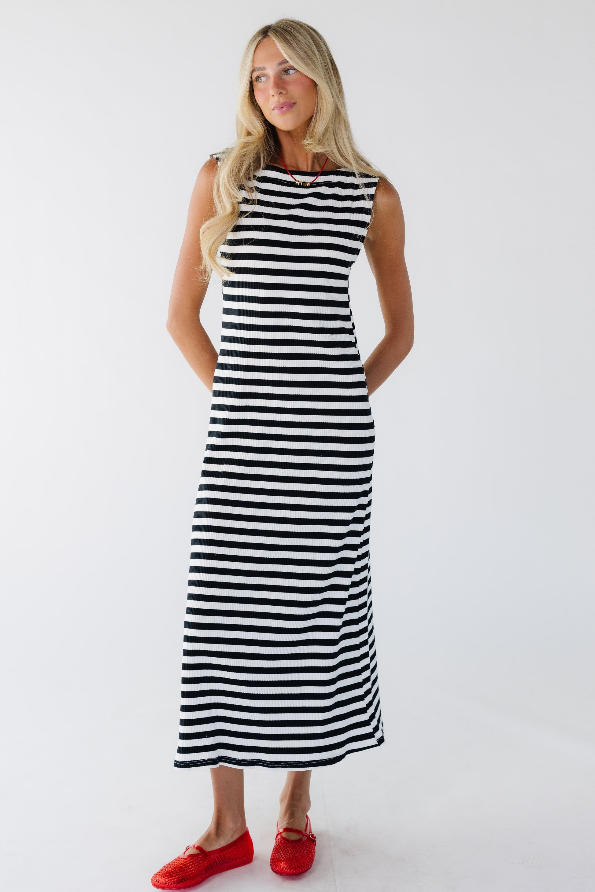 Young woman wearing a close fitting sleeveless black and white stripe midi dress in a midi-maxi length.