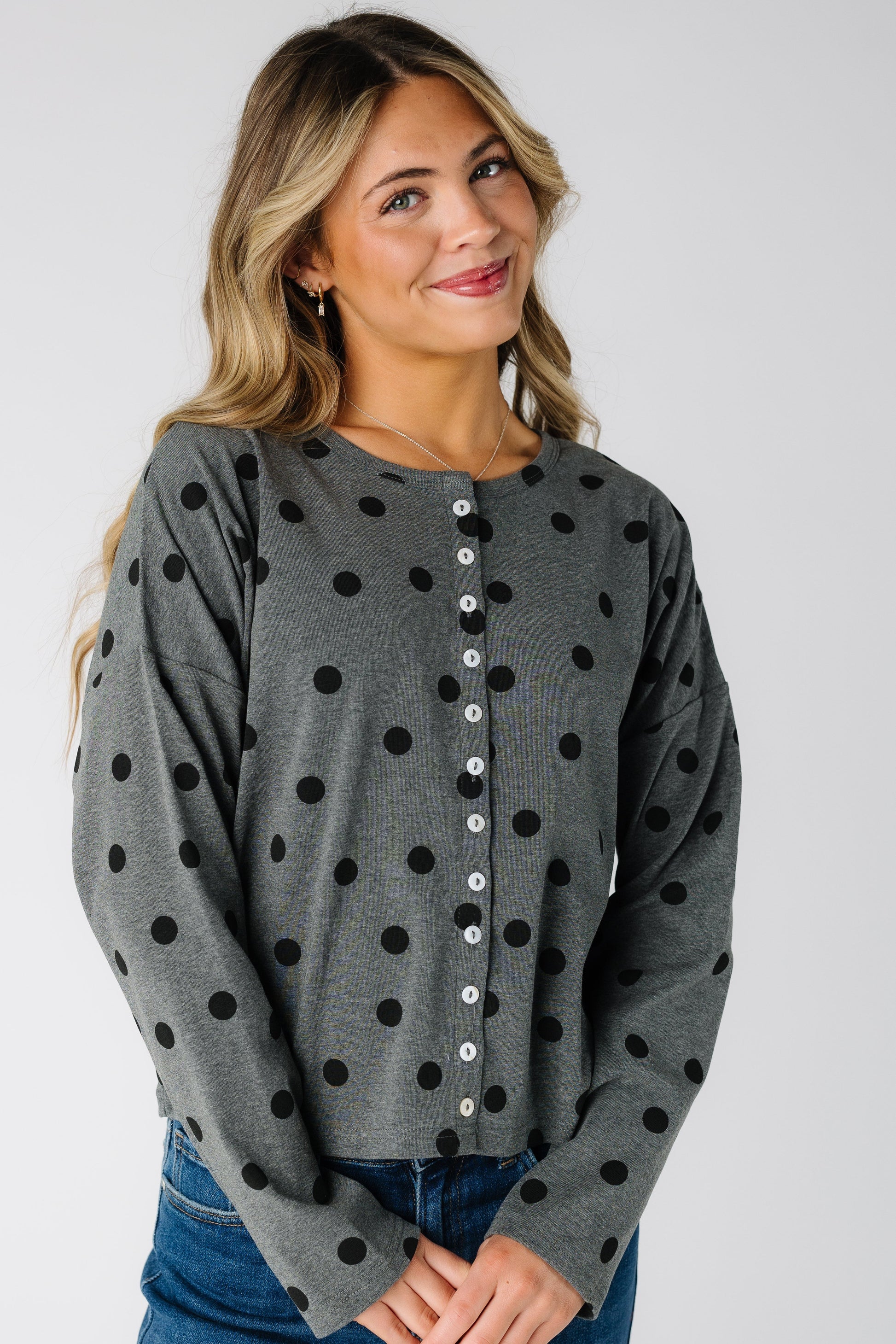 Woman wearing a long sleeve charcoal grey cardigan with black polka dots