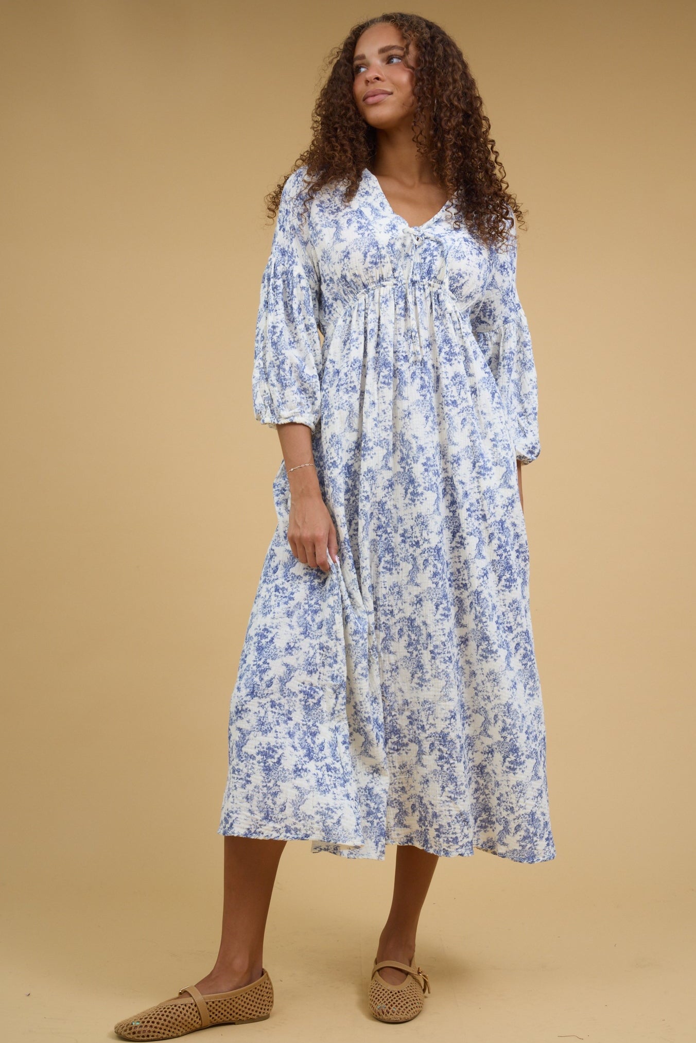 Teenage girl wearing a loose fitting midi dress with and empire waist, V-neckline drop shoulders and half length sleeves.
