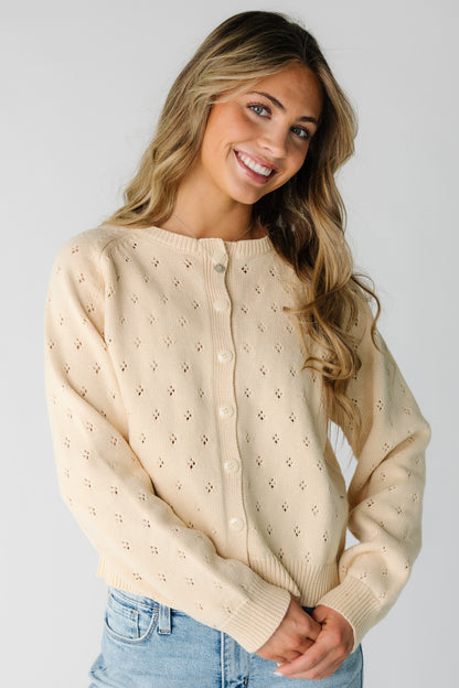 Young woman wearing a cream eyelet knit button down cardigan with long sleeves.