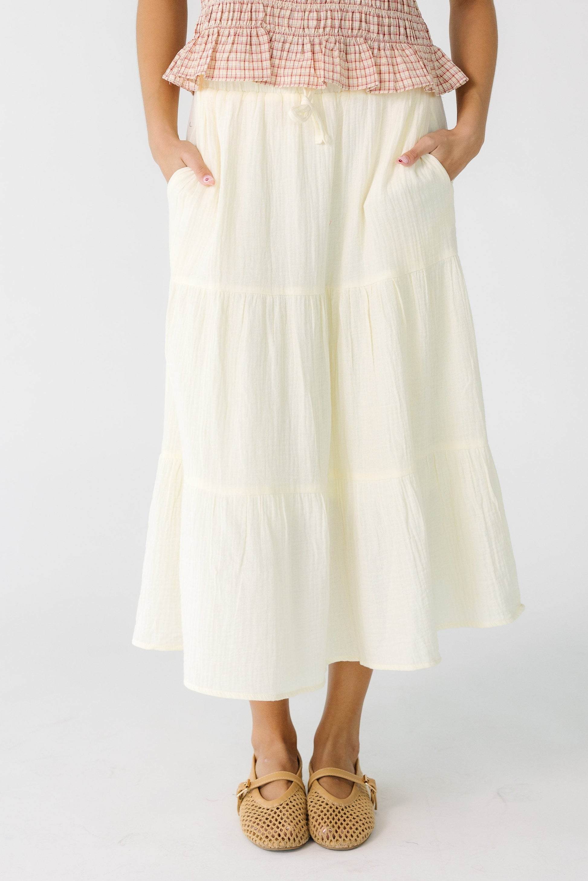 Teen girl wearing a cream gauzy tiered skirt with side pockets and and elastic waistband.