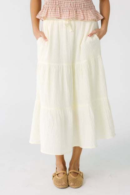 Teen girl wearing a cream gauzy tiered skirt with side pockets and and elastic waistband.