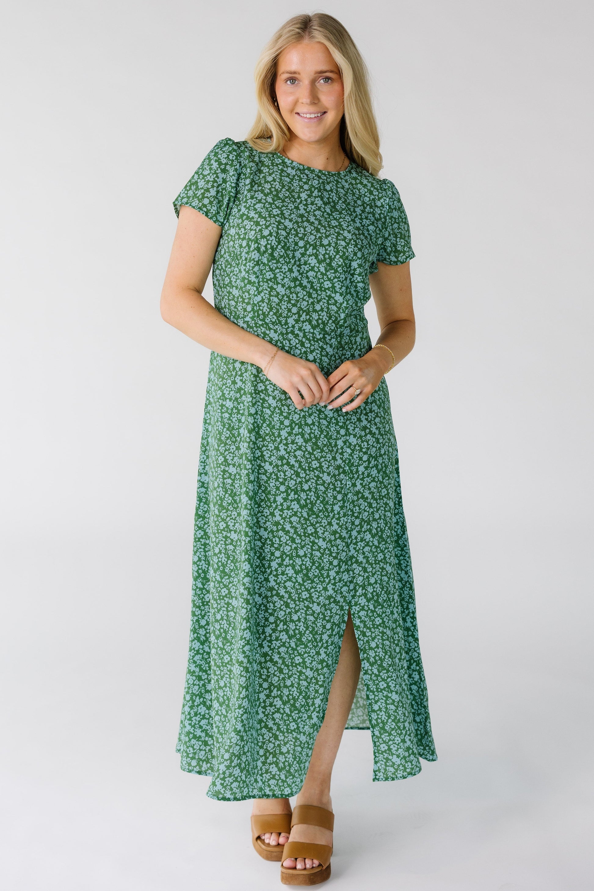 Woman wearing a modest green floral midi dress with a round neckline, short sleeves and a off center front slit to the knee.