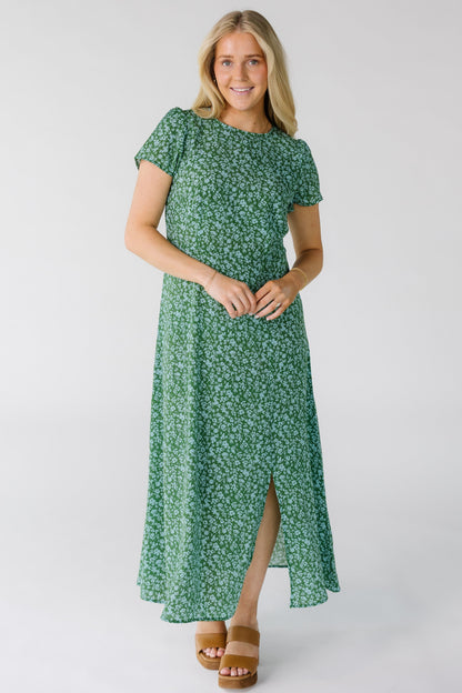 Woman wearing a modest green floral midi dress with a round neckline, short sleeves and a off center front slit to the knee.