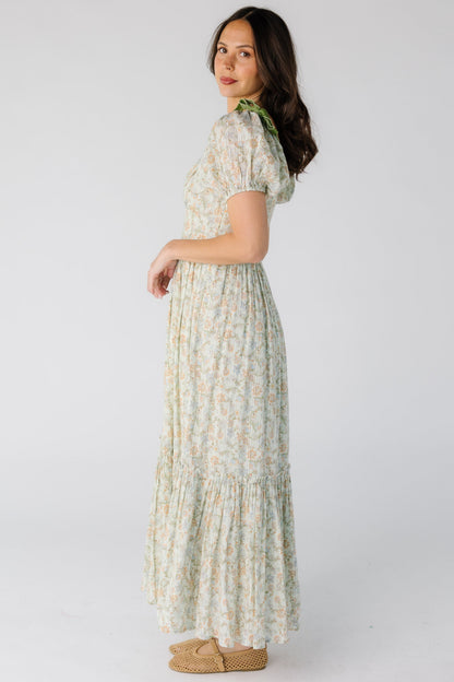 Side view of a woman wearing a green floral print midi-maxi dress with short sleeves and a full gathered skirt with a wide gathered ruffle.