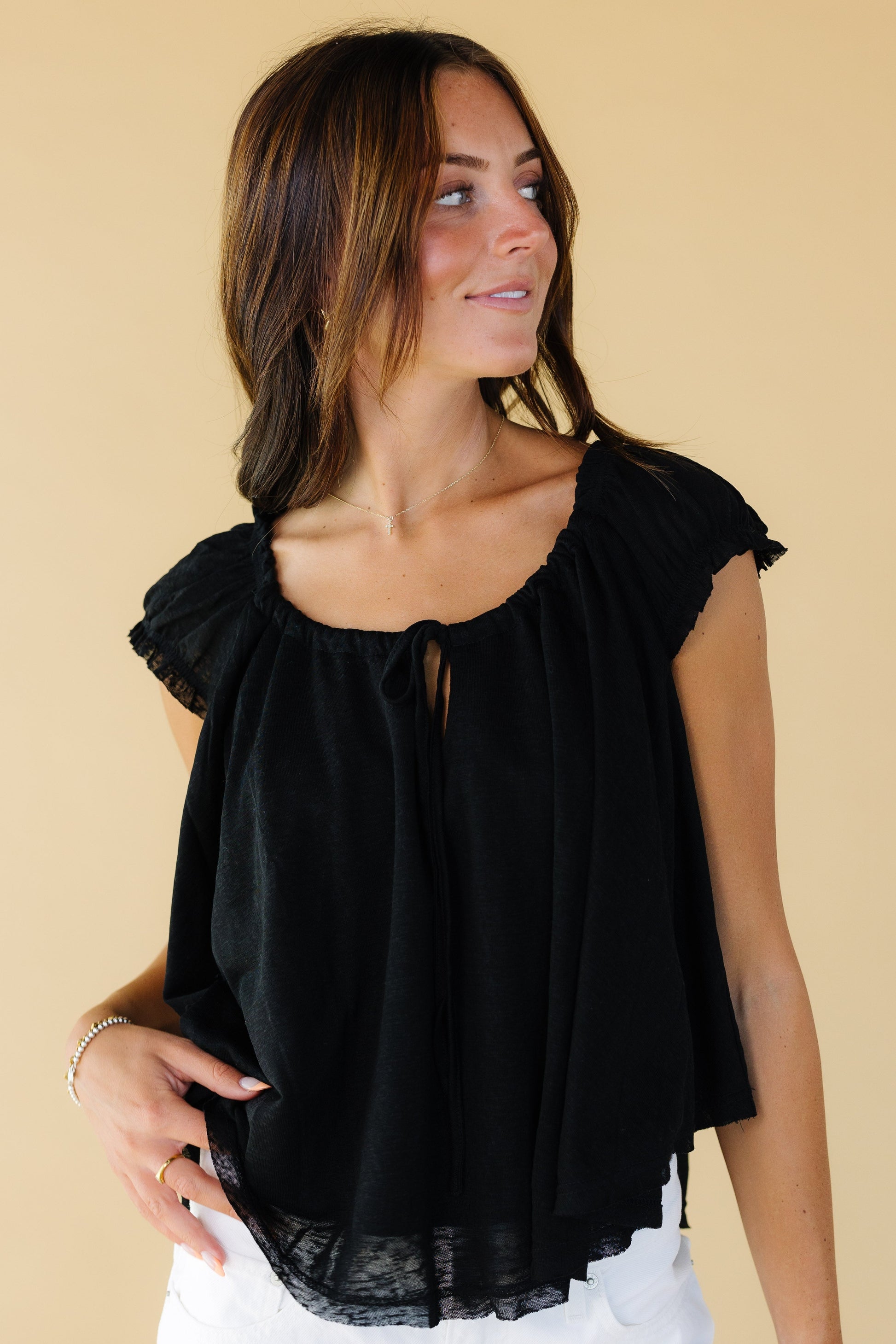 Woman wearing a black lightweight and loose fitting blouse with a drawstring-scoop neckline and short gathered cap sleeves.