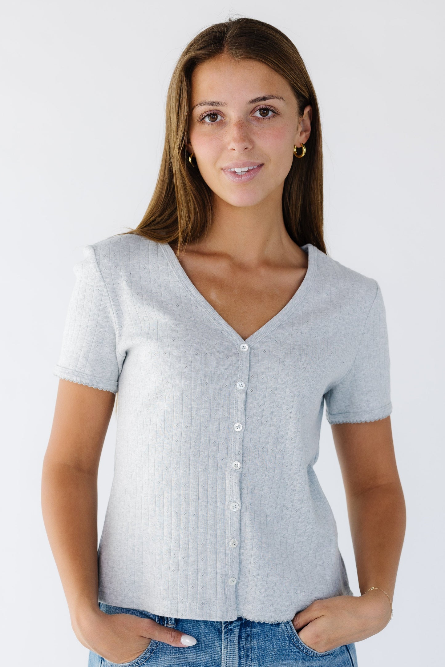 Young woman wearing a heather grey button down top with a V-neckline and short sleeves.