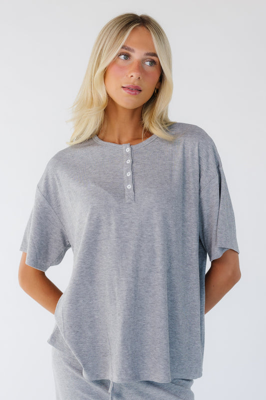 Young woman wearing a modest grey loose fitting top with a short button placket and short sleeves.