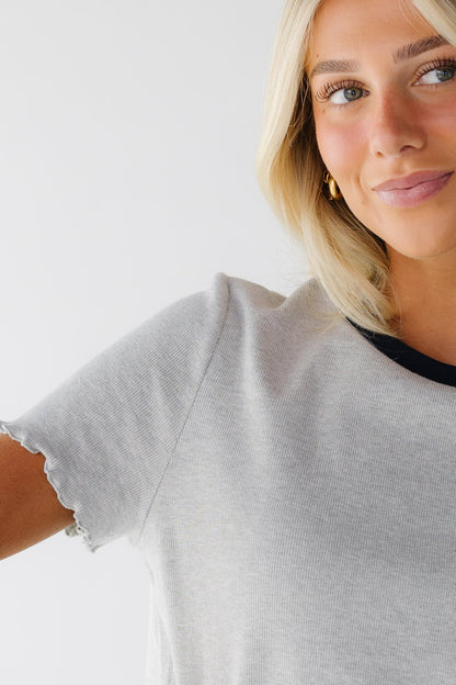 Close view of a woman wearing a grey top with lettuce ruffle hems and a dark crew neckline.