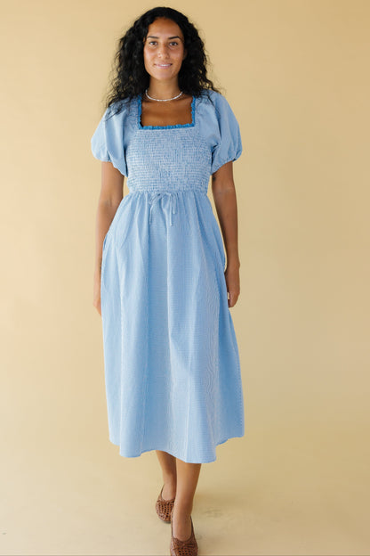 Woman wearing  blue & white gingham midi dress with with a snug smocked bodice, a lace trimmed square neckline, balloon sleeves and a full skirt.
