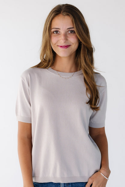Young woman wearing a light grey, lightweight sweater with short sleeves.