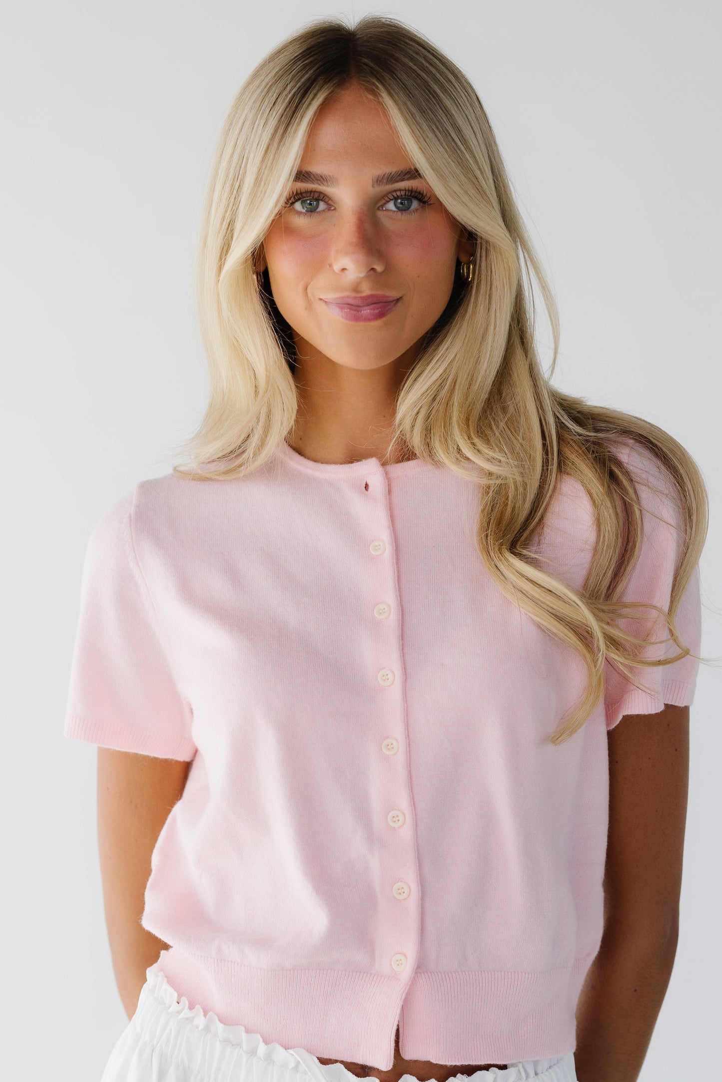 Woman wearing a light pink button down cardigan with short puff sleeves and a round neckline.