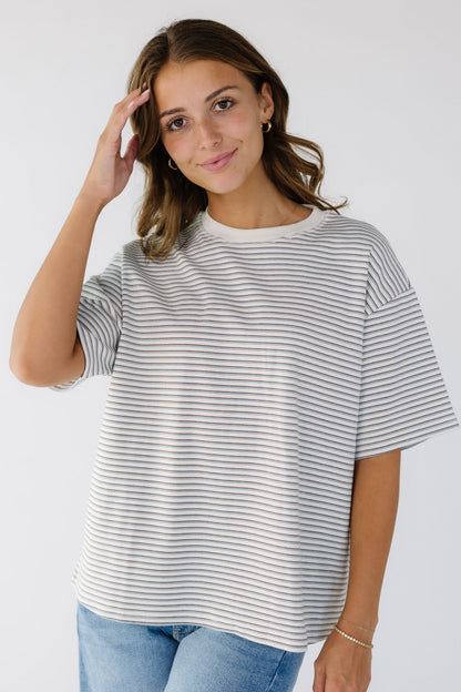 Woman wearing a white loose boxy tee with thin blue & brown stripes with short sleeves ad a white crew neckline.