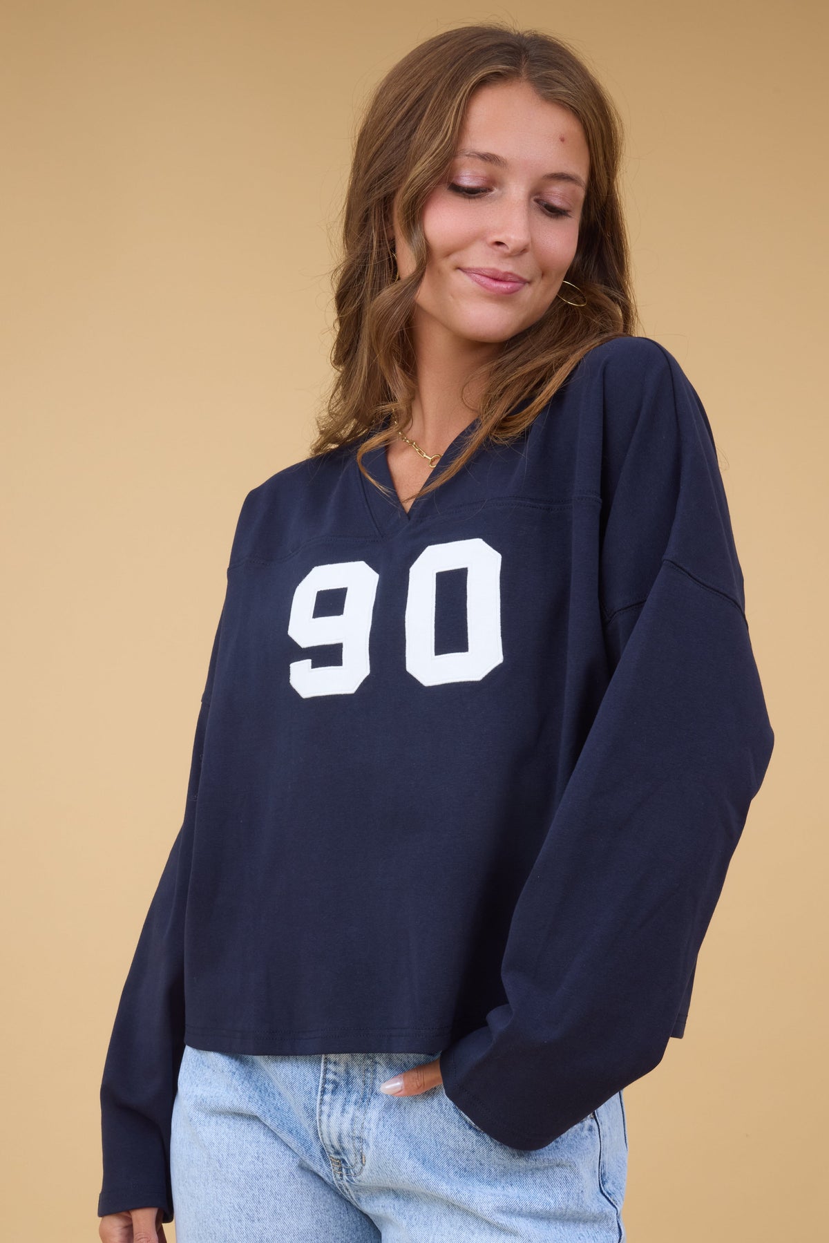 A woman wearing a navy loose fitting tee with a V-neckline, long sleeves and a front number graphic.