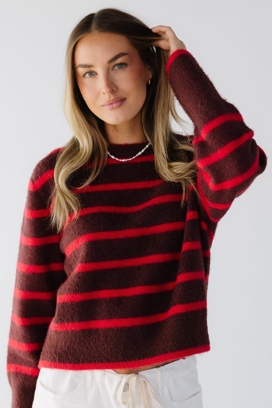 Woman wearing a red & burgunday stripe sweater with very wide ribbed cuffs.