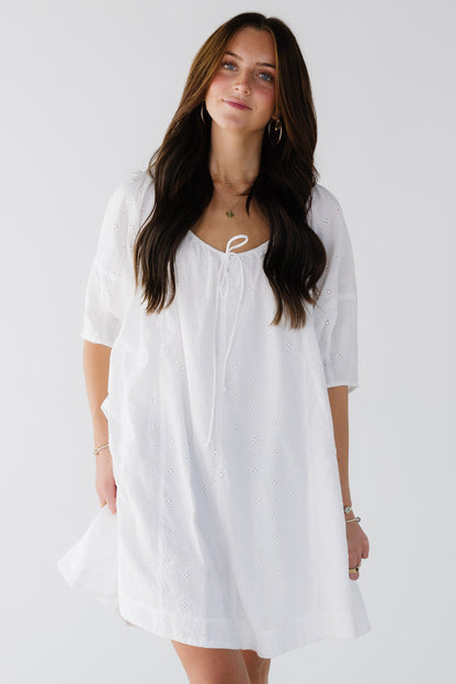 Woman wearing a white eyelet short dreswith elbow length sleeves and drawstring scoop neckline.