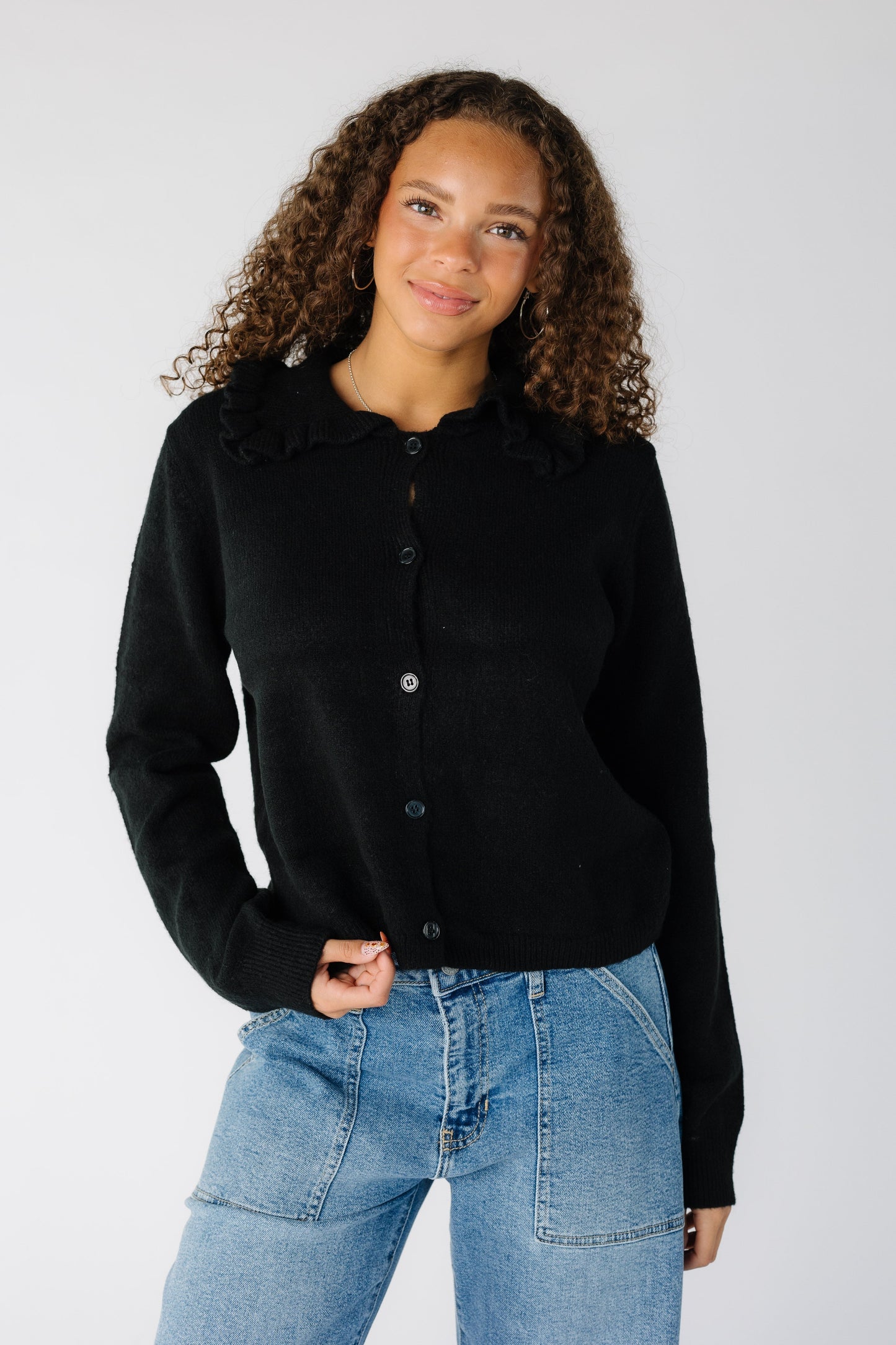 Woman wearing a modest black long sleeve cardigan with matching buttons and wide black collar