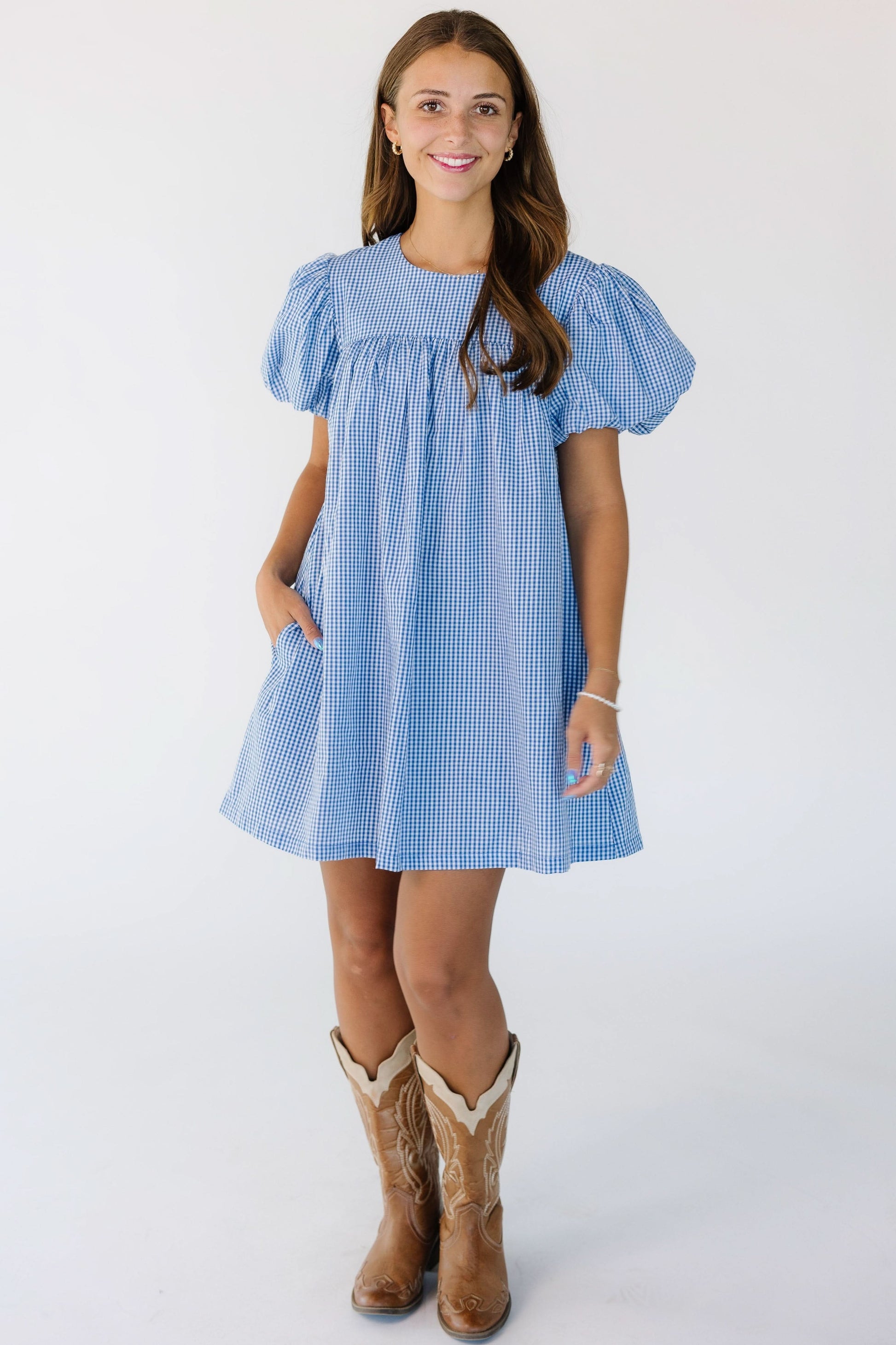 Woman wearing a modest, short, baby doll dress in blue gingham with a round neckline and short balloon sleeves.