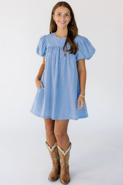 Woman wearing a modest, short, baby doll dress in blue gingham with a round neckline and short balloon sleeves.