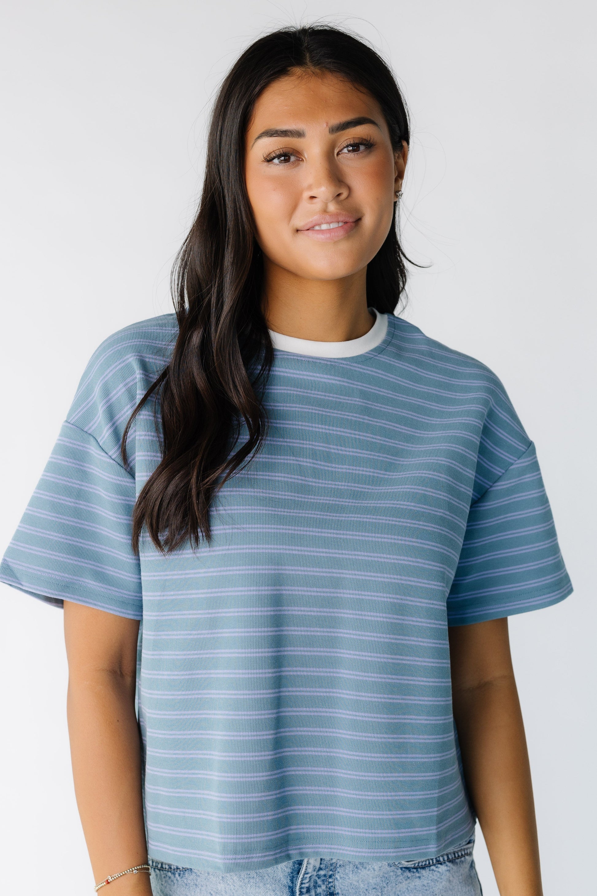 Young woman wearing a modest green tee with blue stripe with a crew neckline in white with short sleeves.