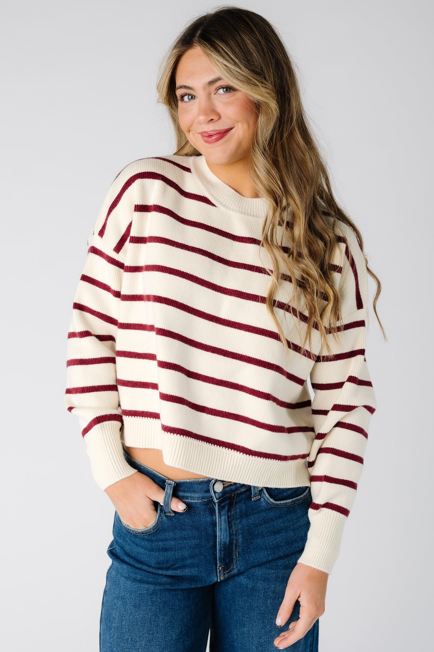 Woman wearing a modest ivory and burgundy stripe sweater with a crew neckline and long sleeves with wide ribbed cuffs