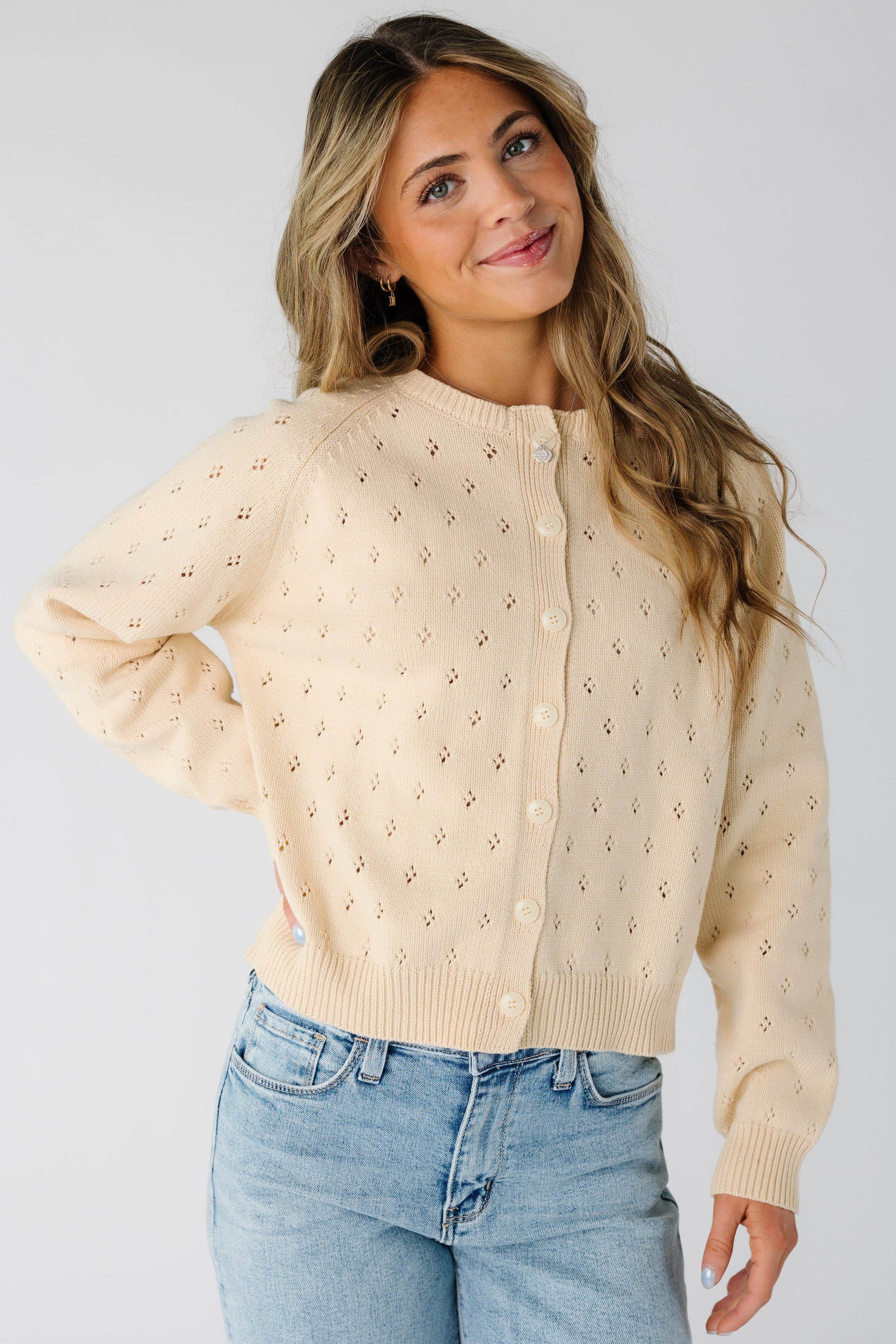 Woman wearing a modest cream eyelet knit cardigan with a crew neckline and long sleeves.