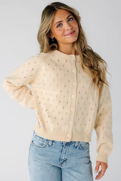Woman wearing a modest cream eyelet knit cardigan with a crew neckline and long sleeves.