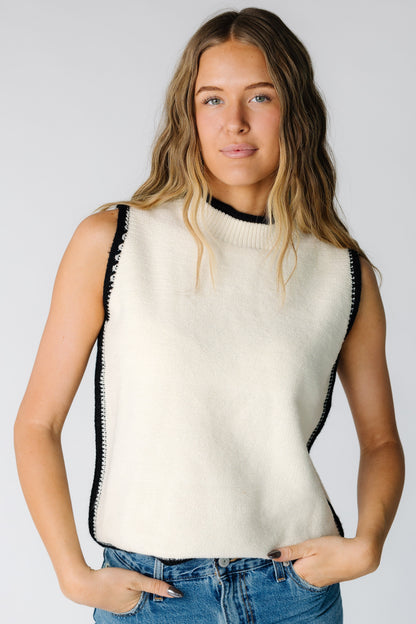 Woman wearing a soft cream sleeveless sweater with black trim
