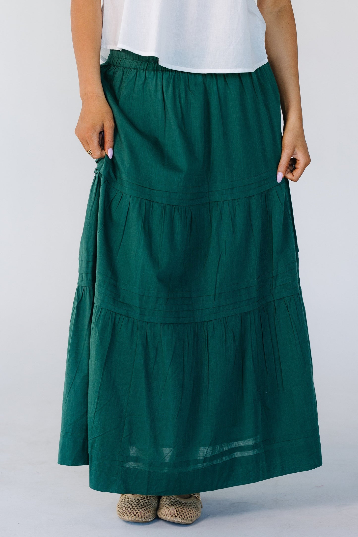Woman wearing a modest green, tiered midi skirt with horizontal pleats,