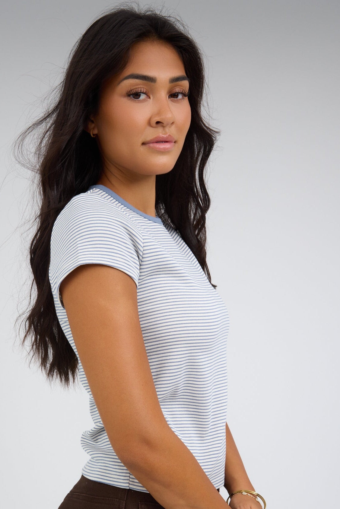 Side view of a woman wearing a white and blue stripe tee with short sleeves.