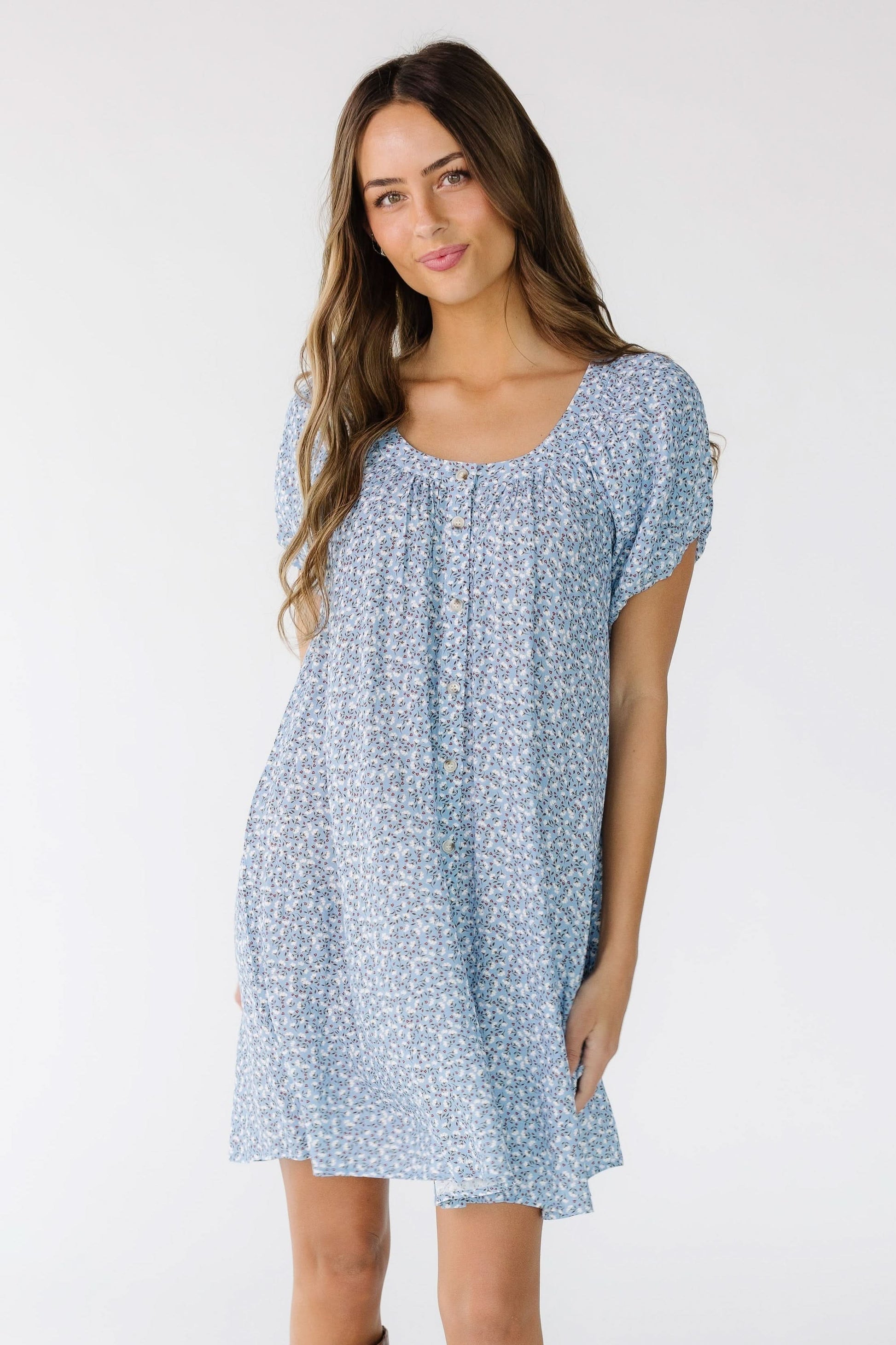 Young woman wearing a  light blue floral print button down dress with a short puff sleeves and a scoop neckline.