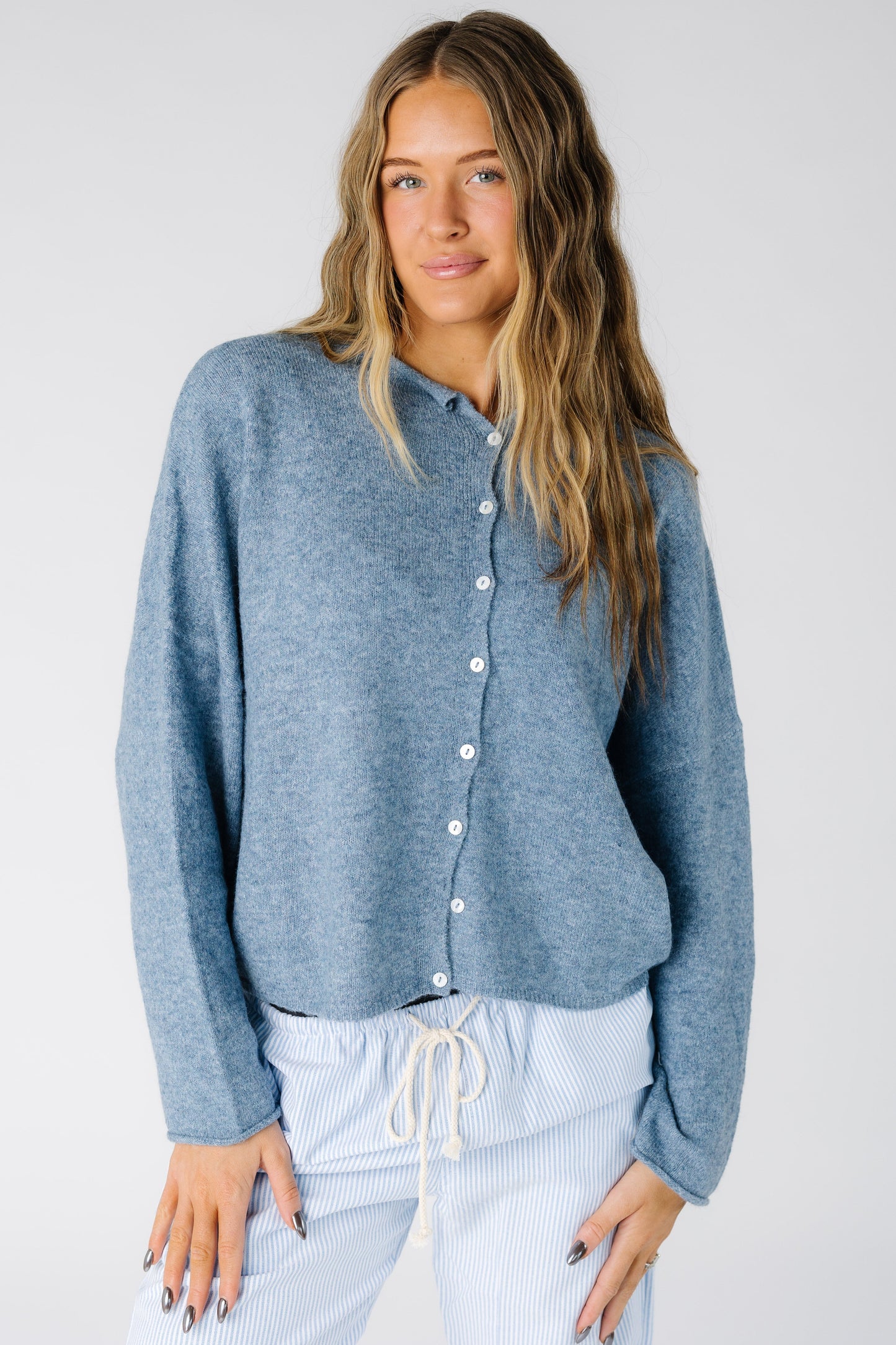 Woman wearing a loose fitting dusty blue cardigan with white buttons and long sleeves